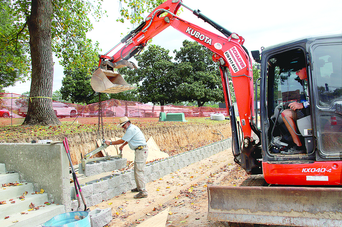Robert Shepherd (left) with Shepherd Builders sets blocks in place for the new retaining wall as Andy Schaefer with Schaefer Construction Services operates an excavator to position them along Oak Street at the Grant County Courthouse square. (Photo: Gretchen Ritchey)