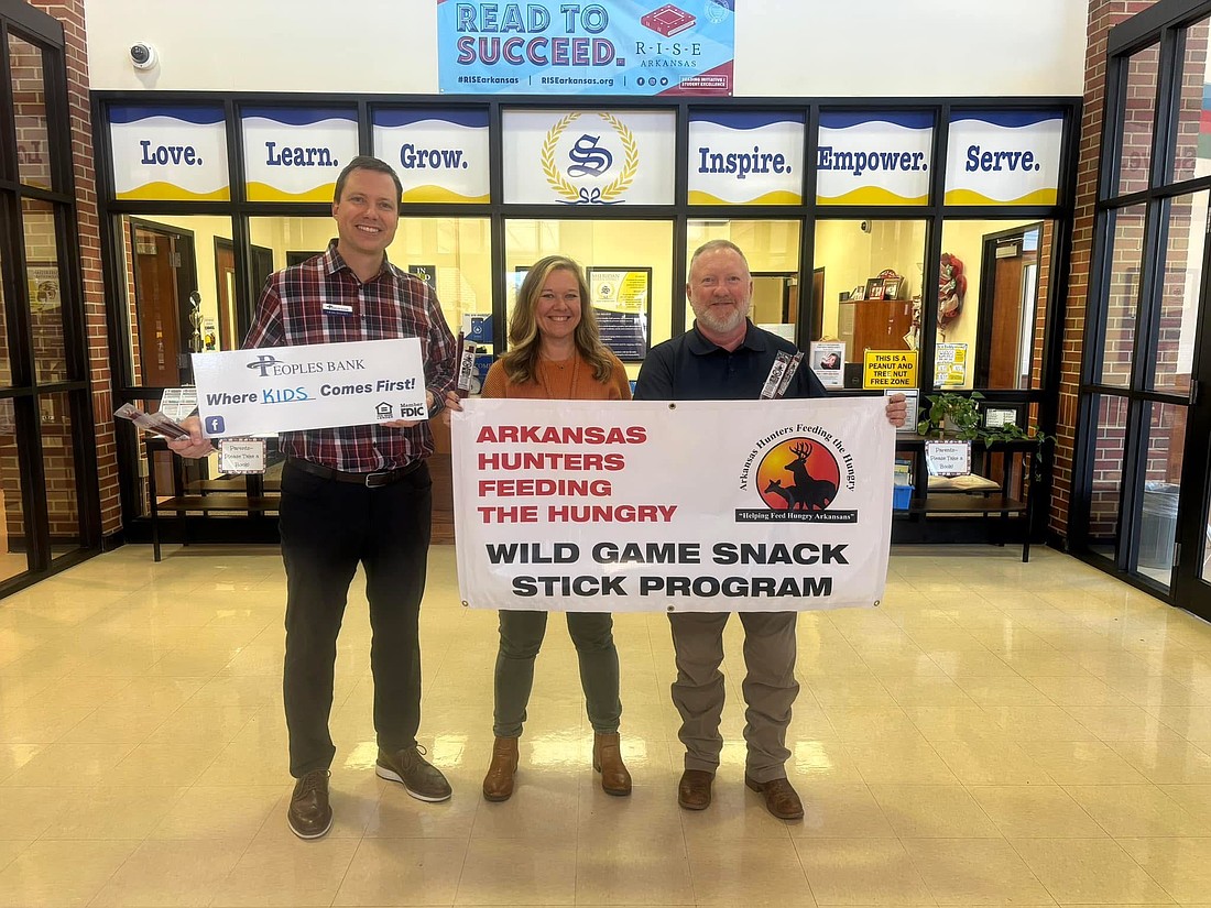 Craig Manatt (left) of Peoples Bank, one of the supporters of Arkansas Hunters Feeding the Hungry organization, stands with Lindsey Bohler, principal at Sheridan Elementary School, and Grant Westmoreland, a local organizer with the group, in this 2024 photograph that was taken when snack sticks were being donated to the school. (Photo: Submitted)